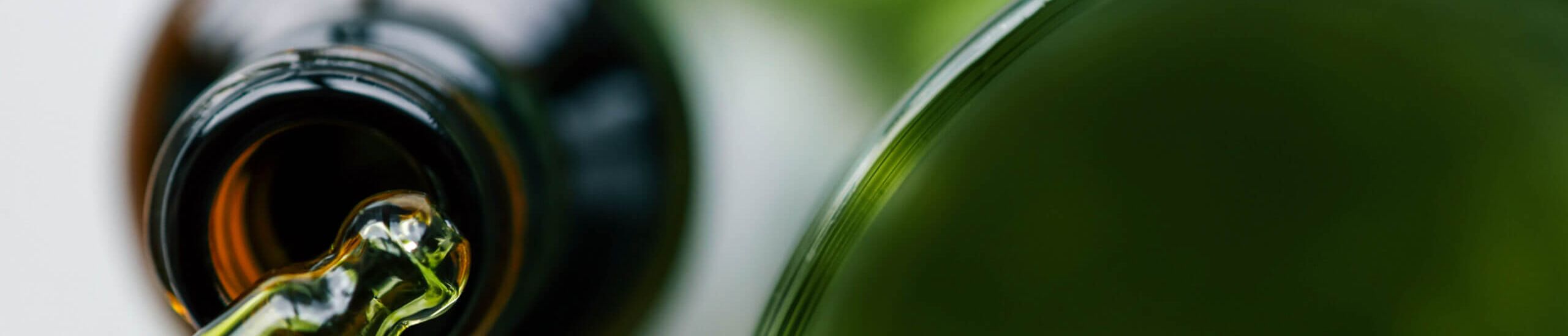 Close-up of a green glass dropper and a brown bottle on a white background with a green leaf. Highlights natural skincare, eco-friendly beauty, and organic wellness products