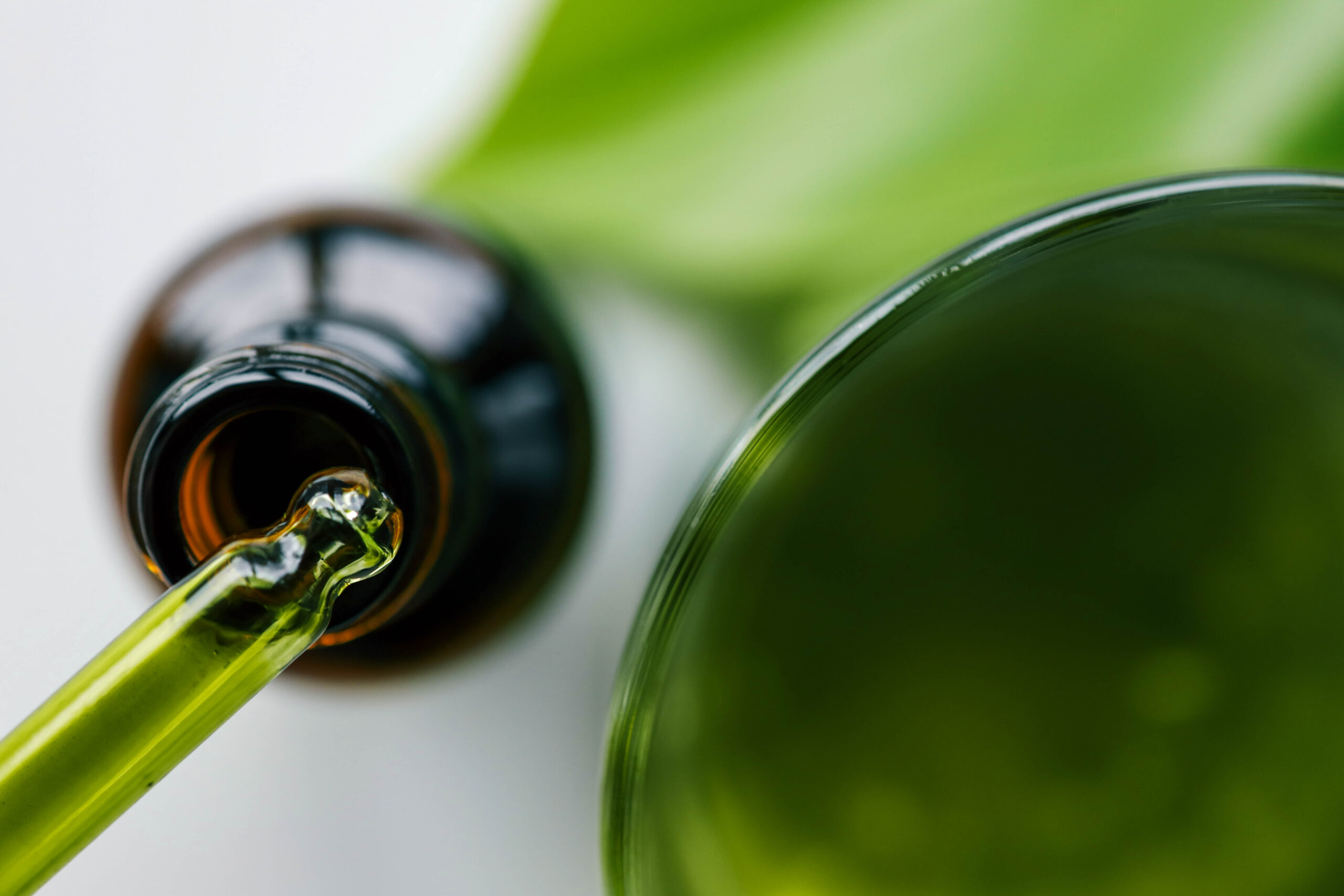 Close-up of a green glass dropper and a brown bottle on a white background with a green leaf. Highlights natural skincare, eco-friendly beauty, and organic wellness products